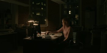 Movie still from “The Assistant” (2019), directed by Kitty Green – A woman sitting in front of a computer at a desk; Extreme Wide shot, High angle