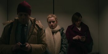 Movie still from “The Assistant” (2019), directed by Kitty Green – Three people sitting in a row waiting for a train; Medium shot, Low angle