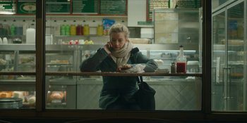 Movie still from “The Assistant” (2019), directed by Kitty Green – A woman sitting at a table in front of a counter; Medium shot, Over the shoulder angle