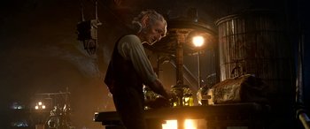 Movie still from “The BFG” (2016), directed by Steven Spielberg – A man standing in front of a table with a lamp; Medium shot, Low angle