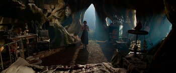 Movie still from “The BFG” (2016), directed by Steven Spielberg – A person standing in a cave with a bed in front of them; Wide shot, Low angle