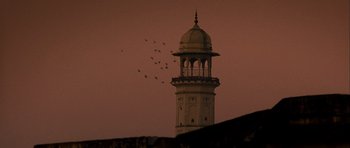 Movie still from “The Best Exotic Marigold Hotel” (2011), directed by John Madden – Birds flying over a tall building at sunset; Extreme Wide shot, Low angle