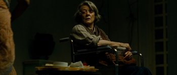 Movie still from “The Best Exotic Marigold Hotel” (2011), directed by John Madden – An older woman sitting at a table in a dark room; Medium shot, Low angle