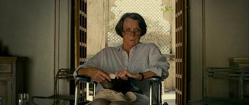 Movie still from “The Best Exotic Marigold Hotel” (2011), directed by John Madden – An older woman sitting in a chair holding a pair of shoes; Medium shot, High angle