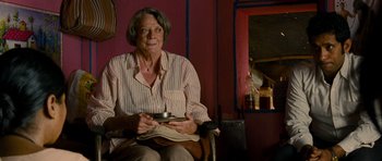 Movie still from “The Best Exotic Marigold Hotel” (2011), directed by John Madden – An older woman sitting in a chair holding a newspaper; Medium shot, Over the shoulder angle