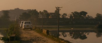 Movie still from “The Best Exotic Marigold Hotel” (2011), directed by John Madden – A car driving down a dirt road next to a body of water; Extreme Wide shot, High angle