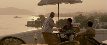 Movie still from “The Best Exotic Marigold Hotel” (2011), directed by John Madden – Two women sitting at an outdoor table under an umbrella; Wide shot, High angle