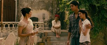 Movie still from “The Best Exotic Marigold Hotel” (2011), directed by John Madden – Two men and a woman sitting on steps in front of potted plants; Medium shot, Over the shoulder angle