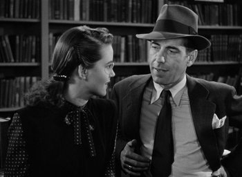 Movie still from “The Big Sleep” (1946), directed by Howard Hawks – An older man wearing a hat and a tie talking to a young woman; Medium shot, Low angle