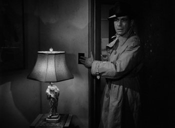 Movie still from “The Big Sleep” (1946), directed by Howard Hawks – A man standing in front of a table with a lamp; Medium shot, Low angle
