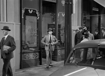 Movie still from “The Big Sleep” (1946), directed by Howard Hawks – A black and white photo of a man walking down the street; Wide shot, Over the shoulder angle