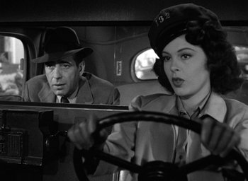 Movie still from “The Big Sleep” (1946), directed by Howard Hawks – A man and a woman driving a car in a black and white photo; Close Up shot, Over the shoulder angle