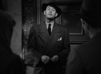 Movie still from “The Big Sleep” (1946), directed by Howard Hawks – A man in a suit and a hat standing in front of another man; Medium shot, Low angle