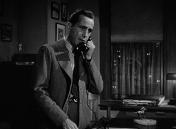 Movie still from “The Big Sleep” (1946), directed by Howard Hawks – A black and white photo of a man talking on a phone; Medium shot, Low angle