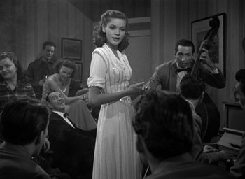 Movie still from “The Big Sleep” (1946), directed by Howard Hawks – A woman in a white dress standing in front of a group of people; Medium shot, Over the shoulder angle