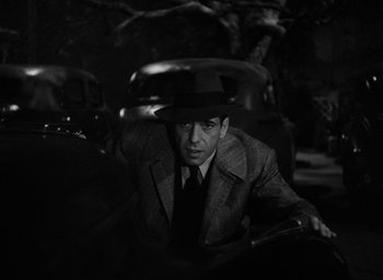 Movie still from “The Big Sleep” (1946), directed by Howard Hawks – A black and white photo of a man in a suit and hat; Close Up shot, Low angle