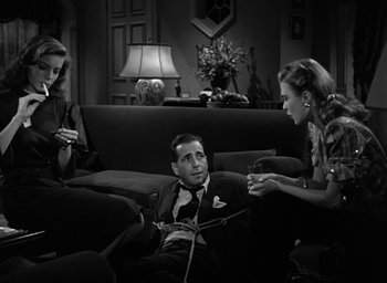 Movie still from “The Big Sleep” (1946), directed by Howard Hawks – A man sitting on the ground next to two women; Medium shot, High angle