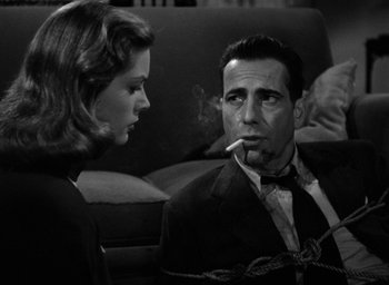 Movie still from “The Big Sleep” (1946), directed by Howard Hawks – A man and a woman sitting on a couch smoking a cigarette; Close Up shot, Low angle