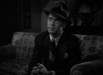 Movie still from “The Big Sleep” (1946), directed by Howard Hawks – A black and white photo of a man in a suit and hat sitting on a couch; Close Up shot, Low angle