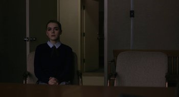 Movie still from “The Blackcoat's Daughter” (2015), directed by Oz Perkins – A woman sitting at a table in front of a door; Medium shot, Over the shoulder angle