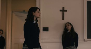 Movie still from “The Blackcoat's Daughter” (2015), directed by Oz Perkins – A woman standing in front of a wall with a cross on the wall; Medium shot, Low angle