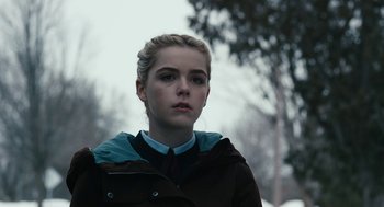 Movie still from “The Blackcoat's Daughter” (2015), directed by Oz Perkins – A young woman in a brown jacket looking at the camera with trees in the background; Close Up shot, Over the shoulder angle
