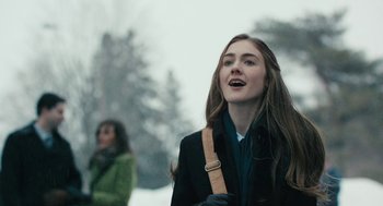Movie still from “The Blackcoat's Daughter” (2015), directed by Oz Perkins – A woman with long brown hair is standing in the snow; Close Up shot, Over the shoulder angle