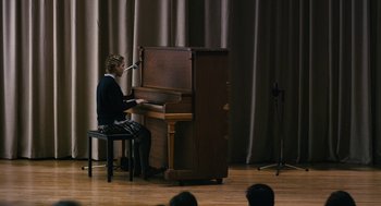 Movie still from “The Blackcoat's Daughter” (2015), directed by Oz Perkins – A person sitting at a piano in front of a curtain; Wide shot, High angle