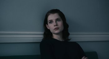 Movie still from “The Blackcoat's Daughter” (2015), directed by Oz Perkins – A woman in a black shirt sitting against a white wall; Close Up shot, Over the shoulder angle