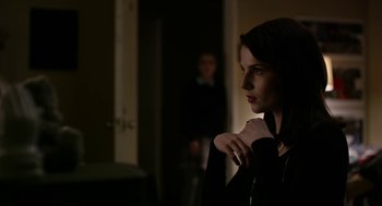 Movie still from “The Blackcoat's Daughter” (2015), directed by Oz Perkins – A woman standing next to a man in a dark room; Medium shot, Over the shoulder angle