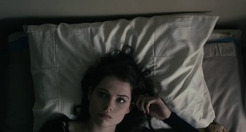 Movie still from “The Blackcoat's Daughter” (2015), directed by Oz Perkins – A woman laying in a bed with her head resting on a pillow; Close Up shot, Overhead angle