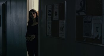 Movie still from “The Blackcoat's Daughter” (2015), directed by Oz Perkins – A woman standing in front of a bulletin board in a dark room; Medium shot, Over the shoulder angle