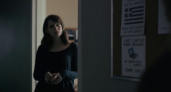 Movie still from “The Blackcoat's Daughter” (2015), directed by Oz Perkins – A woman standing next to a door in a dark room; Medium shot, Over the shoulder angle