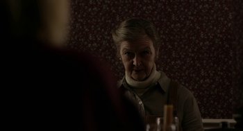 Movie still from “The Blackcoat's Daughter” (2015), directed by Oz Perkins – An older woman looking into a mirror in front of a wall; Close Up shot, Over the shoulder angle