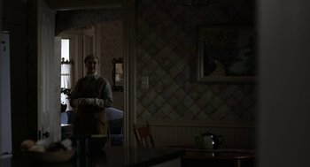 Movie still from “The Blackcoat's Daughter” (2015), directed by Oz Perkins – An older man standing in a room with a tea pot on the table; Wide shot, Over the shoulder angle