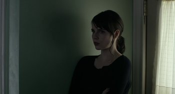 Movie still from “The Blackcoat's Daughter” (2015), directed by Oz Perkins – A woman standing against a wall with her arms crossed; Close Up shot, Over the shoulder angle