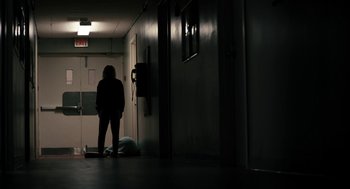 Movie still from “The Blackcoat's Daughter” (2015), directed by Oz Perkins – A person standing in a dark room next to a door; Wide shot, Low angle