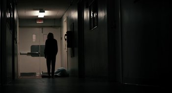 Movie still from “The Blackcoat's Daughter” (2015), directed by Oz Perkins – A woman standing in a dark hallway next to a door; Wide shot, Low angle