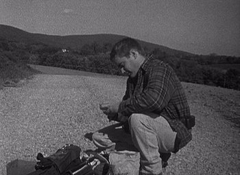 Movie still from “The Blair Witch Project” (1999), directed by Eduardo Sánchez – A man kneeling on the side of a road near a bike; Wide shot, High angle
