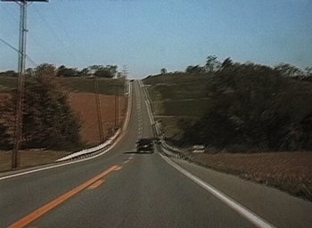 Movie still from “The Blair Witch Project” (1999), directed by Eduardo Sánchez – A car driving down a road on the side of a hill; Extreme Wide shot, High angle