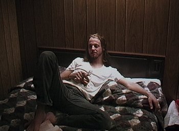 Movie still from “The Blair Witch Project” (1999), directed by Eduardo Sánchez – A man sitting on top of a bed holding a cell phone; Medium shot, High angle