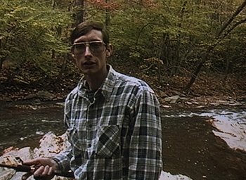 Movie still from “The Blair Witch Project” (1999), directed by Eduardo Sánchez – A man standing in front of a river; Medium shot, High angle