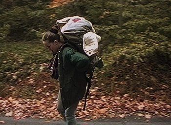 Movie still from “The Blair Witch Project” (1999), directed by Eduardo Sánchez – A woman walking down a road with a backpack on; Wide shot, High angle