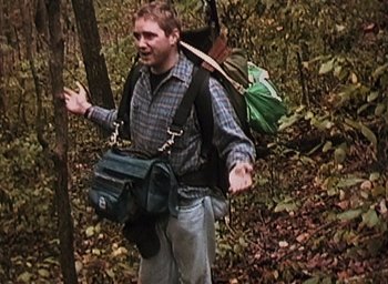 Movie still from “The Blair Witch Project” (1999), directed by Eduardo Sánchez – A man walking through the woods with a backpack on; Medium shot, High angle