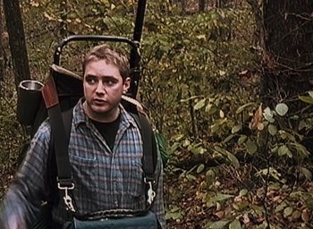 Movie still from “The Blair Witch Project” (1999), directed by Eduardo Sánchez – A man in a plaid shirt with a rifle strapped to his back; Medium shot, High angle