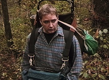 Movie still from “The Blair Witch Project” (1999), directed by Eduardo Sánchez – A man in a plaid shirt with a large backpack; Medium shot, High angle