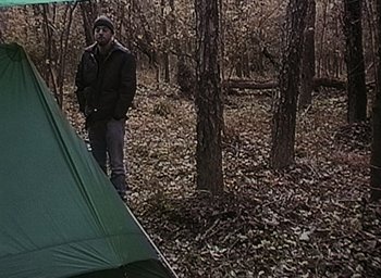 Movie still from “The Blair Witch Project” (1999), directed by Eduardo Sánchez – A man standing next to a tent in the woods; Wide shot, High angle