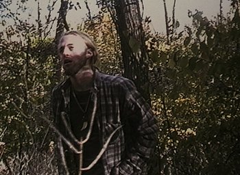 Movie still from “The Blair Witch Project” (1999), directed by Eduardo Sánchez – A man in a plaid shirt standing next to a tree; Medium shot, Low angle