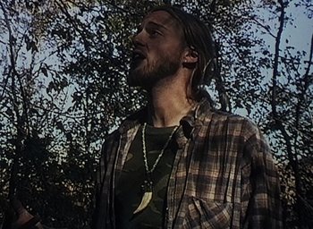 Movie still from “The Blair Witch Project” (1999), directed by Eduardo Sánchez – A man with long hair and a beard is wearing a shirt and a necklace; Medium shot, Low angle