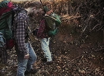Movie still from “The Blair Witch Project” (1999), directed by Eduardo Sánchez – Two people with backpacks walking through the woods; Medium shot, High angle